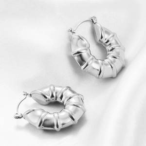 Macro detail of polished silver U-shaped ribbed earrings on white satin background
