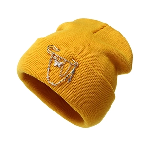 Detail of mustard yellow knit beanie with silver butterfly and cross chain pins