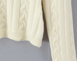 Gros plan détaillé sur la maille torsadée blanc cassé et l'ourlet côtelé du pull en tricot