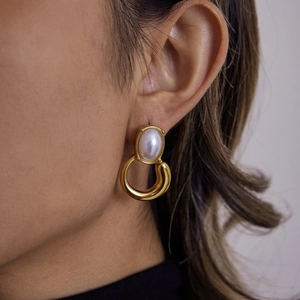 Elegant gold titanium steel earring with an oval faux pearl on a model's ear