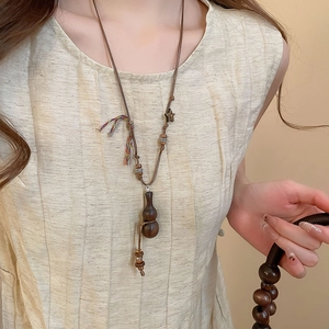 Detailed close-up of a vintage ethnic necklace featuring a wooden gourd pendant on a beige linen shirt