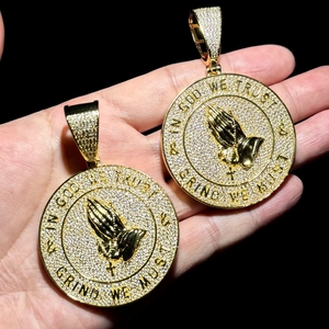 Macro shot of gold hip-hop shield pendant with prayer hands and In God We Trust engraving