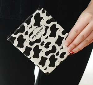 Close-up of a cow print passport holder with black text being held by a hand