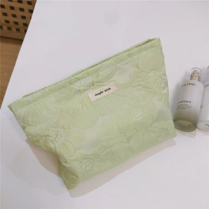 Detail view of light green jacquard fabric makeup bag with embossed floral texture and label