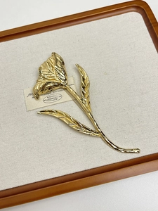 Detail shot of golden tulip flower brooch with polished finish on a rustic linen background
