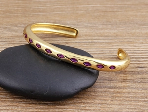 Detail of an 18k gold-plated open cuff bracelet with purple marquise-cut zircons on a pebble