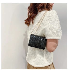 Quilted black patent leather heart bag with gold chain strap shown on a model