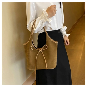 Brown frosted leather tote bag with beige bow accent worn by a model in a warm interior