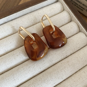 Close-up of golden U-shaped earrings with caramel acrylic resin pendants on velvet