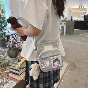 Détail d'un sac bandoulière en toile bleu clair avec breloque poupée dans un café