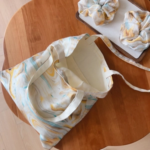 Detail of canvas tote bag with marble print and matching hair scrunchies on wooden table