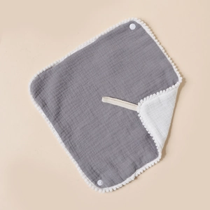 Close-up of baby cotton muslin bib with white pom-poms, grey fabric, and snap button