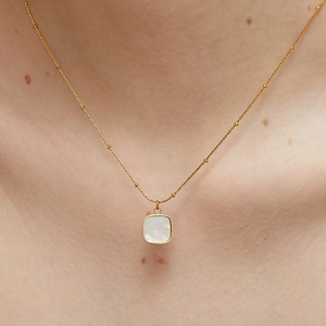 Golden satellite chain necklace with square white shell pendant worn on the neck