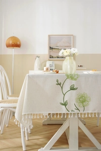 Detail of embroidered green floral patterns and white fringe on a beige linen tablecloth