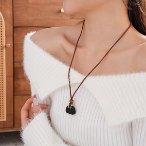 Detail of faux stone bag pendant with gold handle and wood beads on brown leather cord