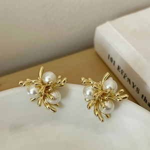 Detailed shot of 18k gold plated pearl earrings placed on a white ceramic plate