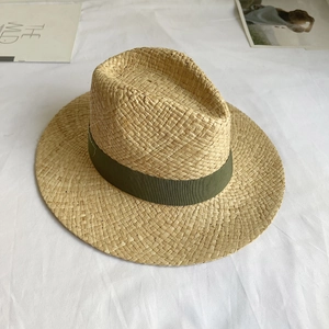Detail of hand-woven natural raffia straw hat with dark green ribbon on white fabric