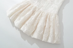 Detailed close-up of white jacquard fabric with delicate embroidery and ruffle hemline