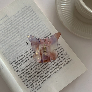 Detailed close-up of a purple and pink gradient butterfly hair claw on a vintage book
