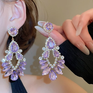 Macro detail of elegant gold chandelier earrings with purple water-drop crystals