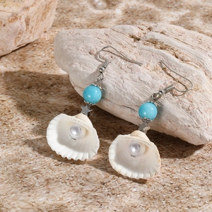 Detail of shell earrings with blue beads and pearls on beach-style stone background