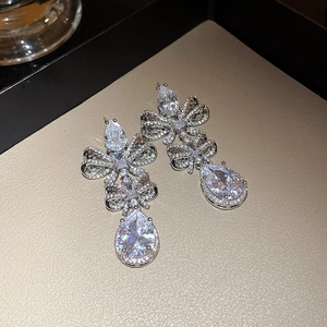 Close-up of sparkling silver ribbon bow and pear-cut teardrop earrings on a tray