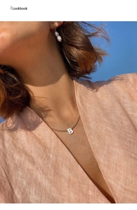 Close-up of golden letter B pendant necklace on model under bright blue sky