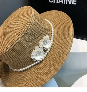 Detail of tan straw sun hat featuring white pearl headband and delicate silk flowers