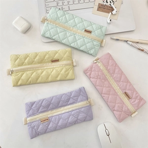 Close-up of quilted pastel pencil cases in four colors on a white office desk setup