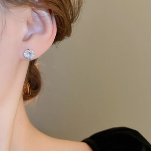 Close-up of a single round-cut zircon stud earring on ear with silver prong setting