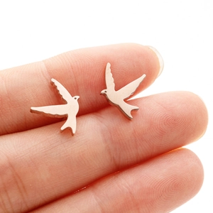Close-up of rose gold swallow bird stud earrings held on a fingertip for size