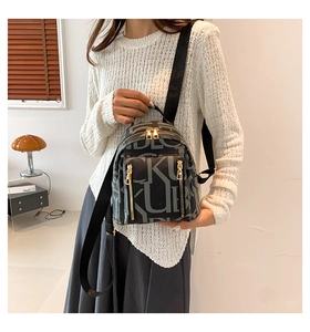 Detail of dark grey backpack with white letter print and gold zipper held by a model
