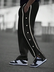 Detail view of black side-button track pants with white stripes and snap fasteners