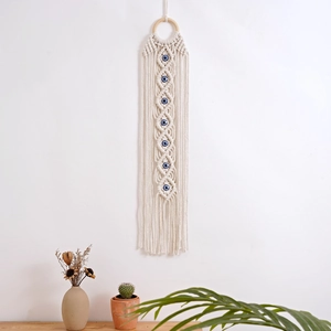 Detail of hand-woven cotton macrame wall hanging with blue evil eye beads and fringes
