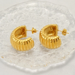 Detailed close-up of golden C-shaped stainless steel earrings with vertical striped texture