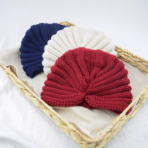 Close-up of three knitted beanies in navy, beige, and red inside a woven basket