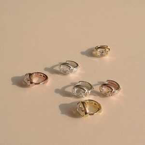 Detail of oval-cut zircon huggie earrings in gold, silver, and rose gold finishes