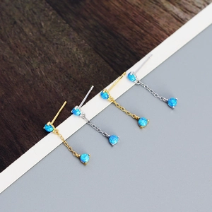 Detail of silver and gold tassel earrings featuring vibrant blue opal stones on wood