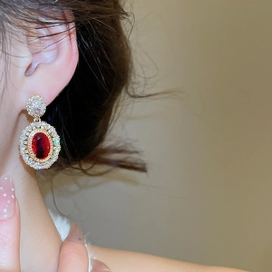 Close-up of gold-plated oval red zircon drop earrings with white stone cluster detailing