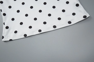 Detail von weißem Stoff mit schwarzen Punkten zeigt Saumnaht und Stricktextur