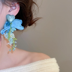 Detail of a floral tassel earring with blue fabric heart and acrylic beads on a model