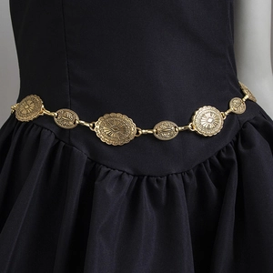 Detail of vintage bohemian gold chain belt with engraved metal charms on a black dress