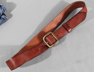 Close-up of brown leather belt with vintage brass buckle on denim fabric background