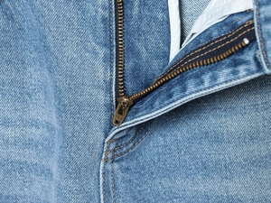 Detailaufnahme des hochwertigen YKK-Metallreißverschlusses und des blauen Denim-Stoffs der Jeans