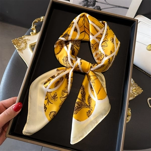 Carré de soie jaune élégant avec motifs floraux présenté sur un plateau noir chic