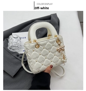Close-up of beige quilted crossbody bag with pearl bow charm on a grey blazer background