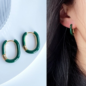 Detail of green enamel U-shaped earrings on model and white background with gold plating