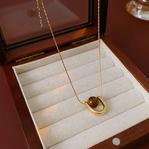 Detail of gold titanium steel necklace with U-shaped tiger eye pendant in a wooden jewelry box