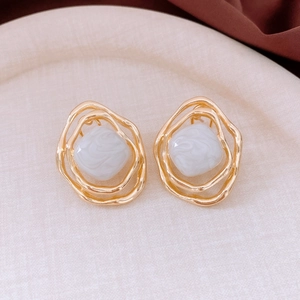 Close-up of gold geometric earrings with grey marbled resin inlay on beige display