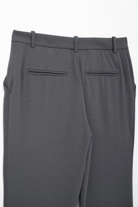 Detail view of high-waisted dark grey suit trousers featuring belt loops and welt pockets